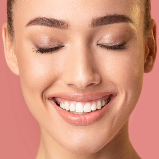 Aesthetic Clinic in Ilford and Canterbury close up portrait of smiling woman with flawless skin against dark peach pink backdrop